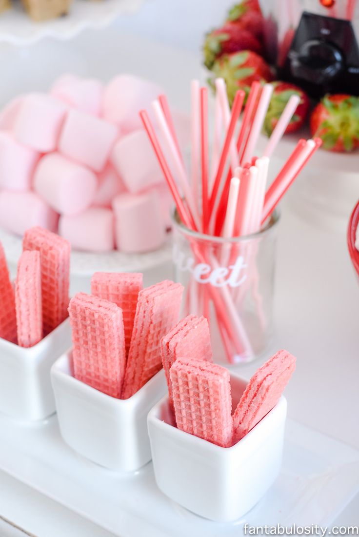 pink and white marshmallows in small bowls on a table with candy sticks