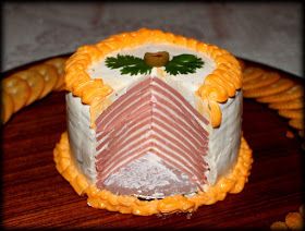 a fancy cake with meat and cheese on it sitting on a wooden table next to crackers