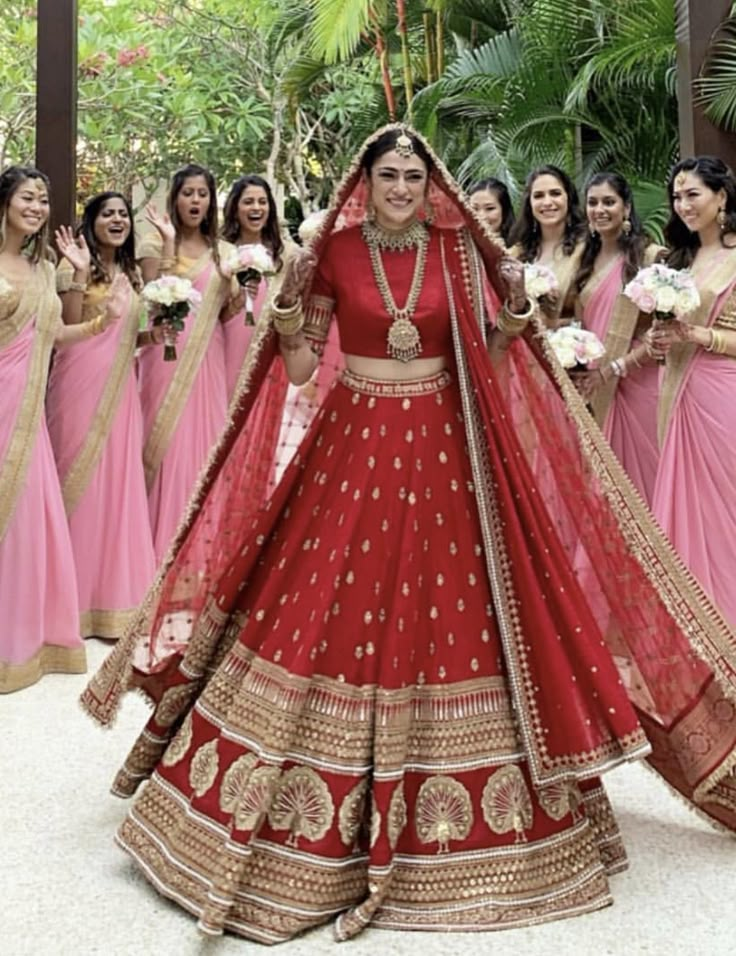 a woman in a red and gold bridal gown standing with her bridesmaids