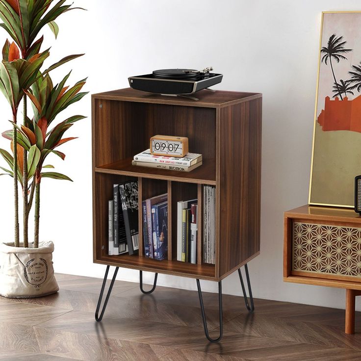 a wooden book shelf with books on it next to a potted plant and an old record player