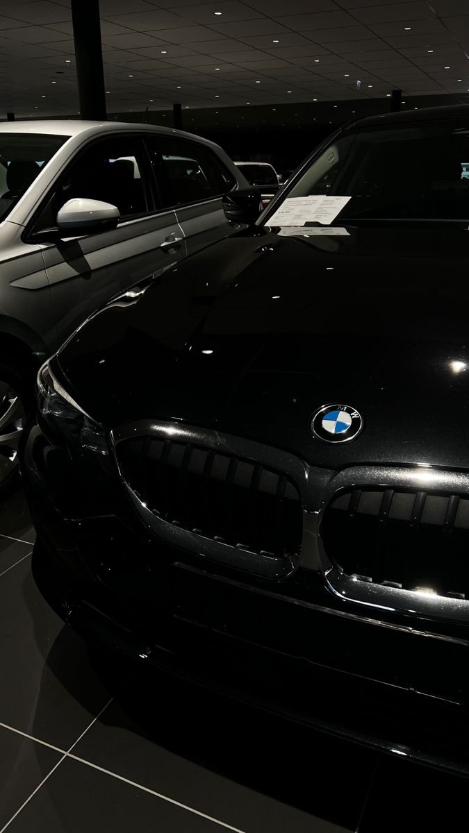 two cars parked next to each other in a room with tile flooring and black walls