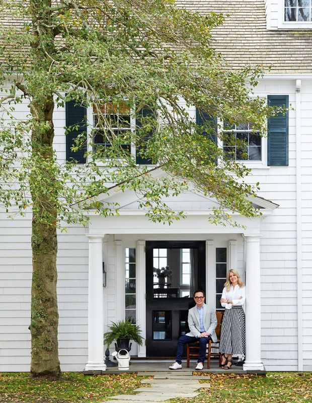 a man and woman sitting on a bench in front of a white house