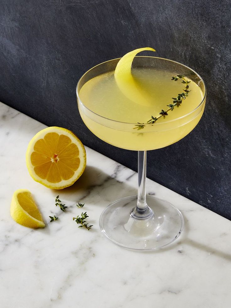 a glass filled with lemonade and garnish next to an orange slice on a marble counter