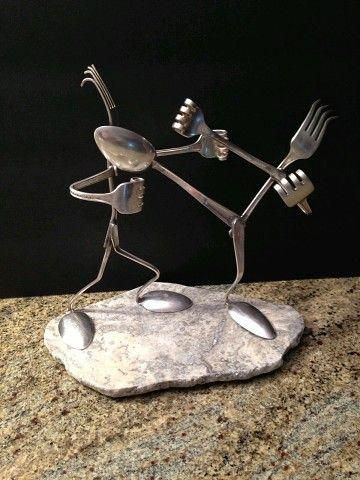 a metal sculpture with forks and spoons on it's legs, sitting on top of a rock