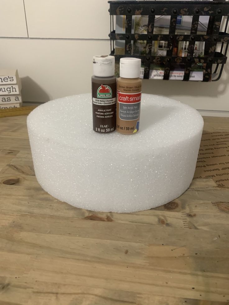 two bottles of paint sitting on top of a white foam covered round table with wood flooring