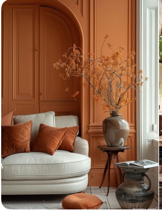 an orange living room with white couches and brown accents on the walls, along with a vase filled with dried flowers