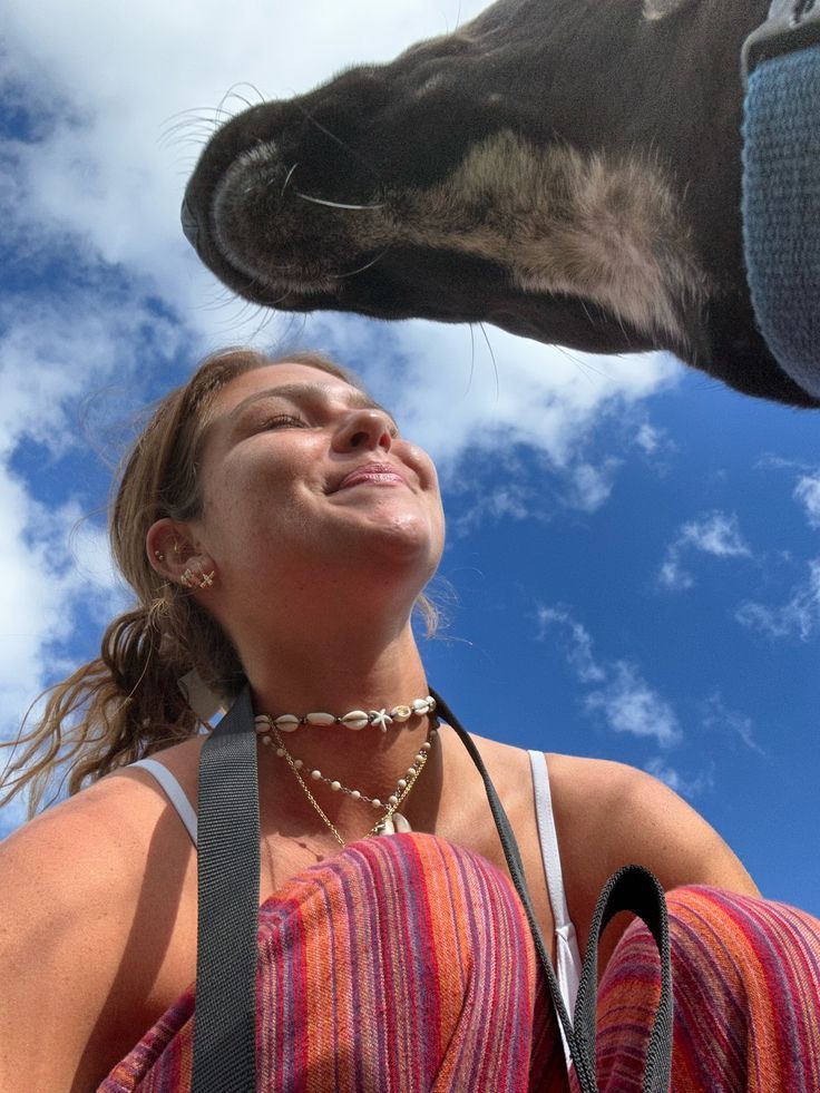 a woman standing next to a horse with her mouth open and the sky in the background