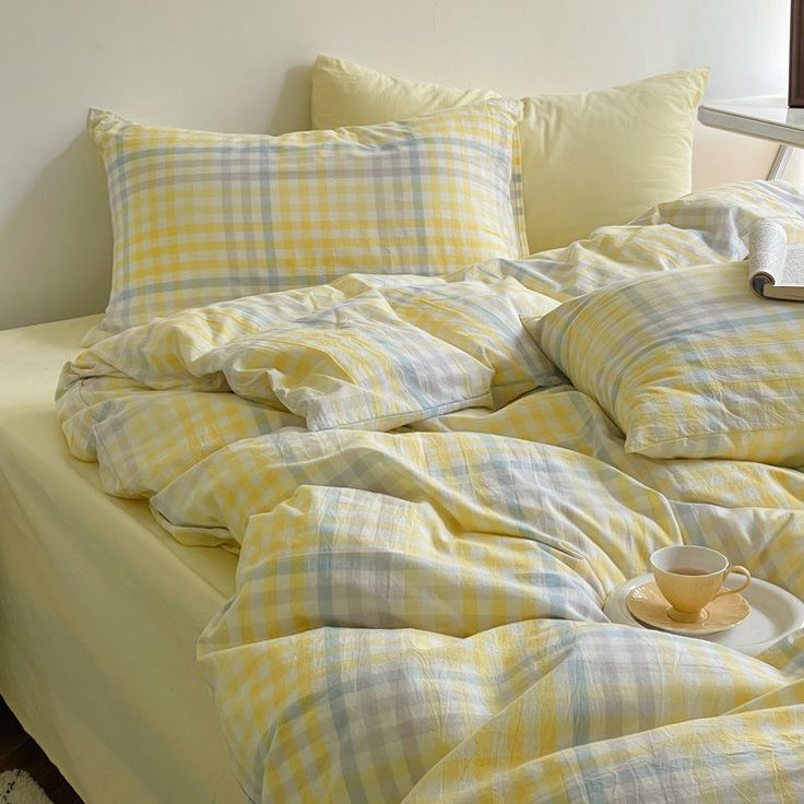 an unmade bed with yellow and white plaid comforter, pillows and a cup on it