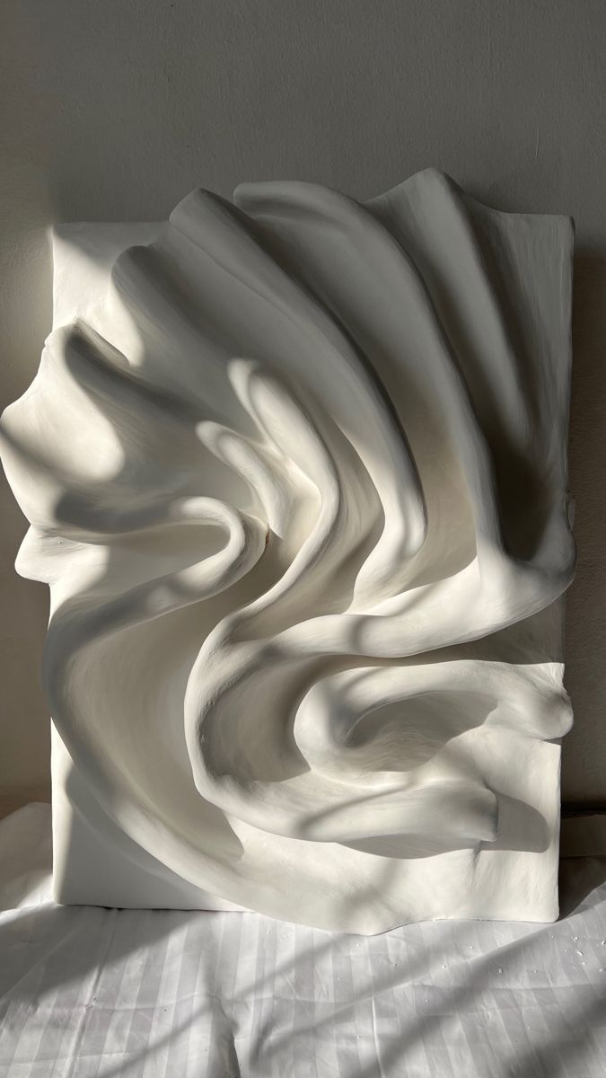 a white sculpture sitting on top of a bed next to a pillow covered in sheets