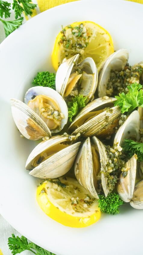 a white plate topped with clams and broccoli next to lemon wedges