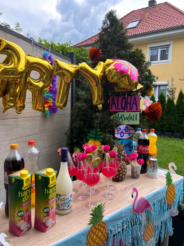 a party table with balloons, pineapples and drinks on it in front of a house