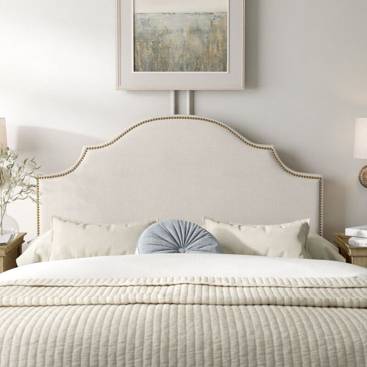 a bed with white pillows and yellow headboard in front of a painting on the wall