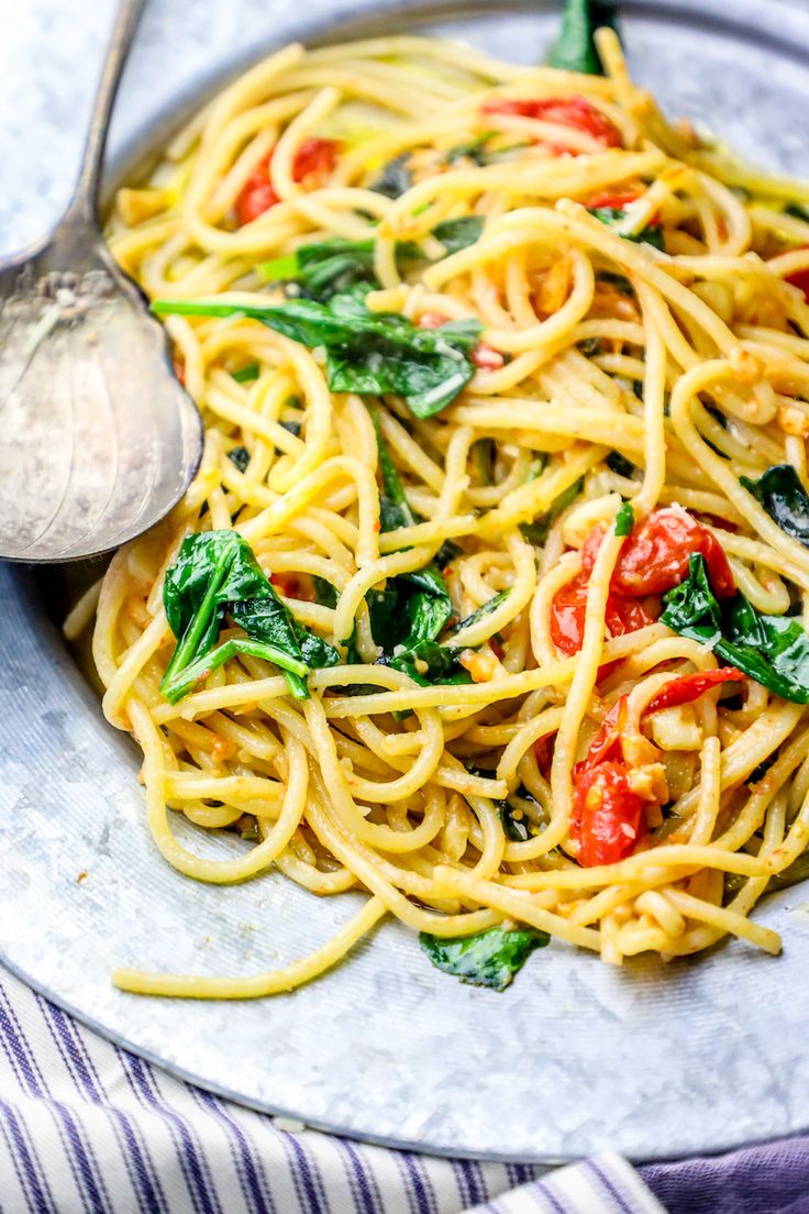 a plate of pasta with spinach, tomatoes and other toppings on the side