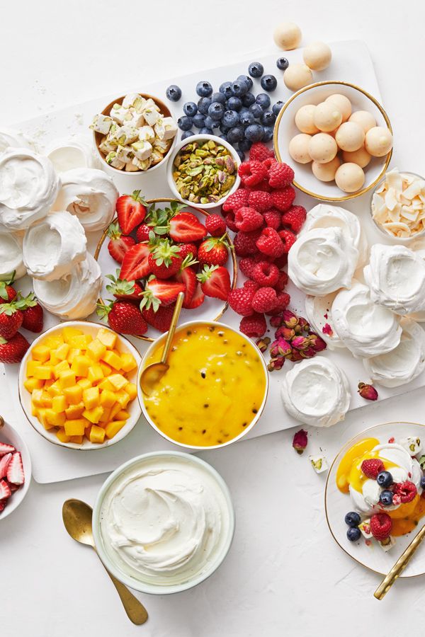 various fruits and dips are arranged on a platter, including strawberries, blueberries, raspberries, peaches, custard