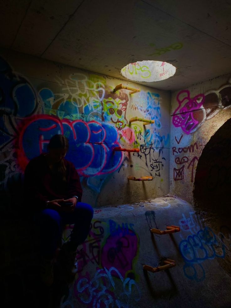 a man sitting in a dark room with graffiti on the walls and ceiling above him