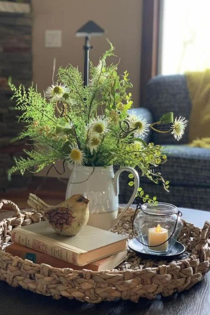 a tray with flowers, candles and books on it sitting on a table in front of a couch