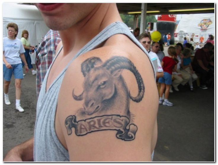 a man with a goat tattoo on his arm in front of an outdoor area full of people