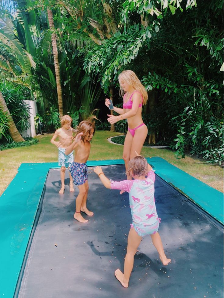 three young children playing on an inflatable trampoline with two adults and one child