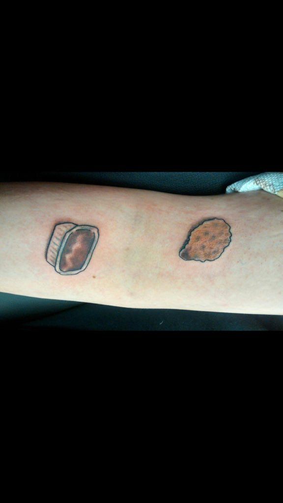 a person's arm with two tattoos on it and some food in the middle