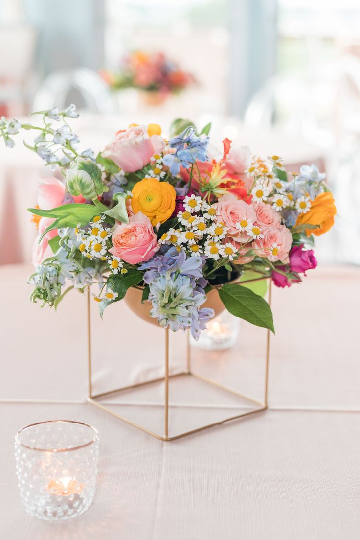 a vase filled with lots of colorful flowers on top of a white table cloth covered table