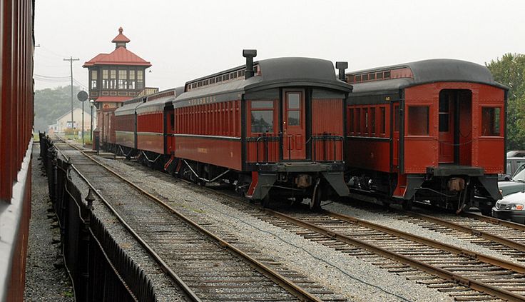 a red train traveling down tracks next to a traffic light and tall tower in the background