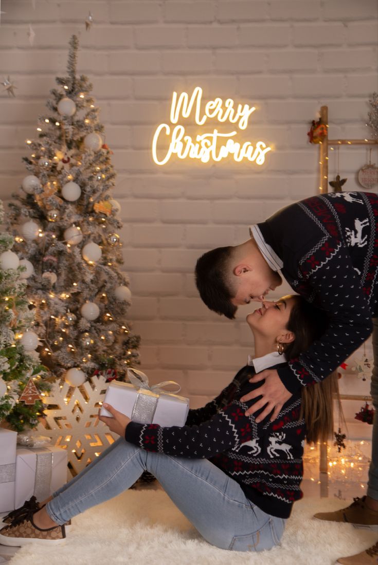 a couple kissing in front of a christmas tree