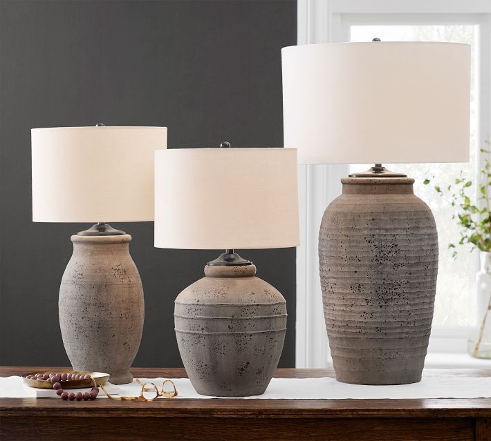 three vases on a table with lamps in front of them and one is empty