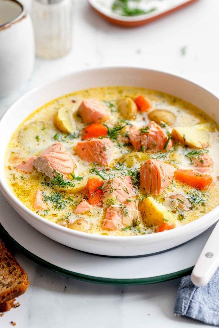 a bowl of salmon and potato soup on a plate next to some slices of bread