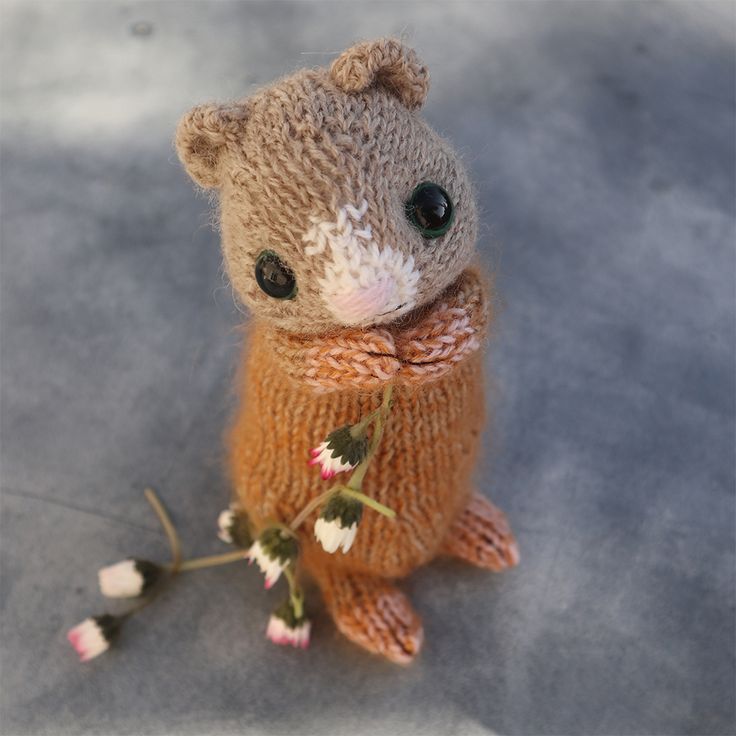 a knitted teddy bear sitting on the ground with flowers in it's paws