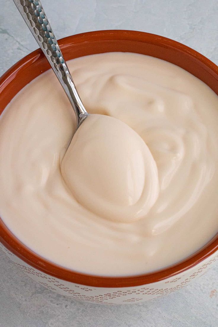 a bowl filled with cream sitting on top of a white counter next to a spoon