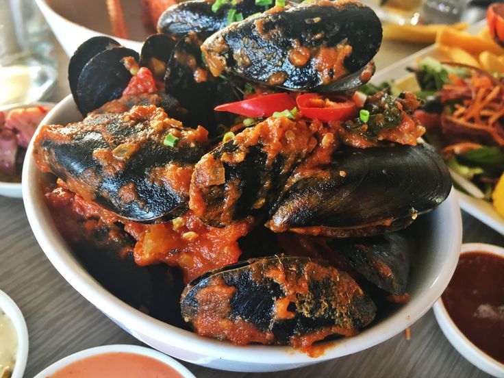 a bowl filled with mussels and sauce on top of a table next to other dishes