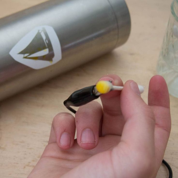 a hand holding a tiny black and yellow object in it's left hand next to a water bottle