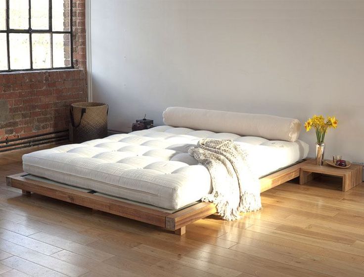 a bed sitting on top of a hard wood floor next to a brick wall and window