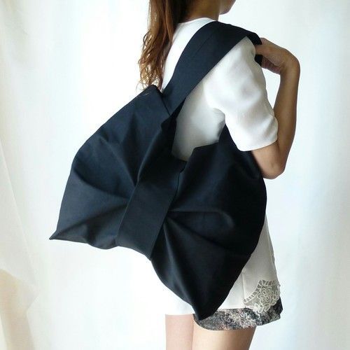 a woman is holding a black bag with a large bow on it's back