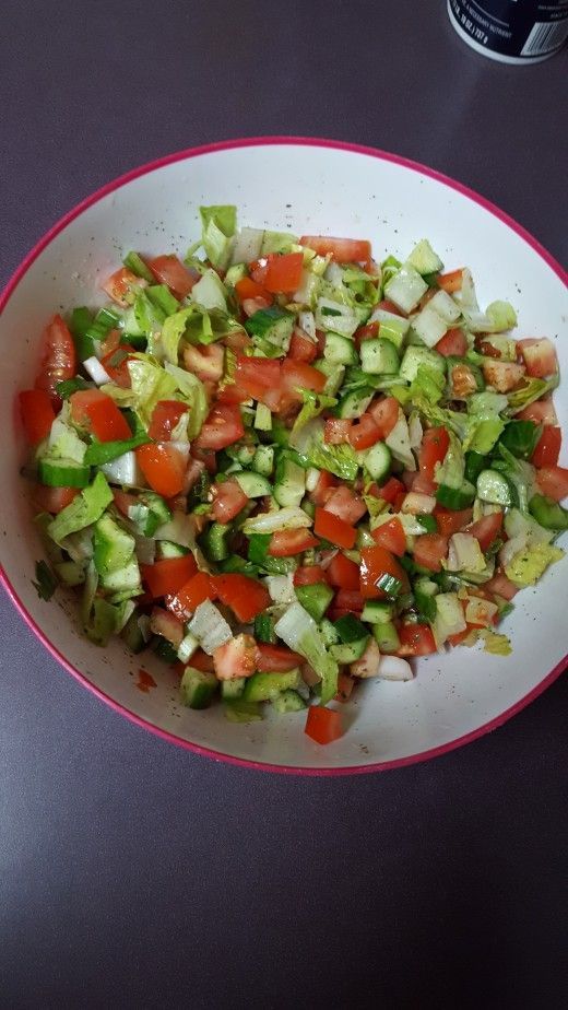 a white plate topped with cucumber and tomato salad next to a glass of water