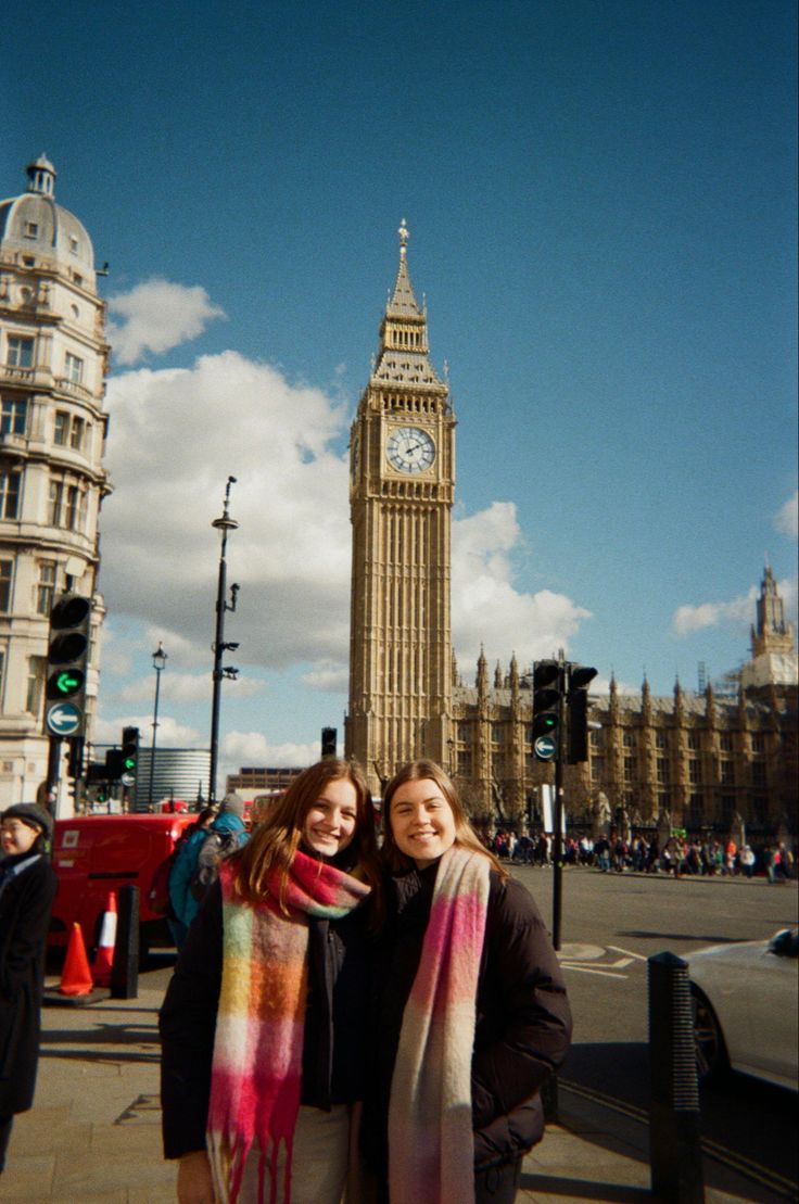 two women standing next to each other in front of a clock tower