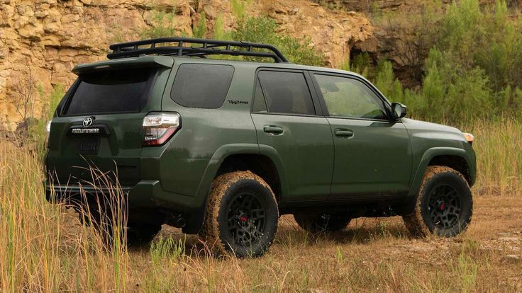 a green four - doored toyota 4runner parked in the grass near a cliff