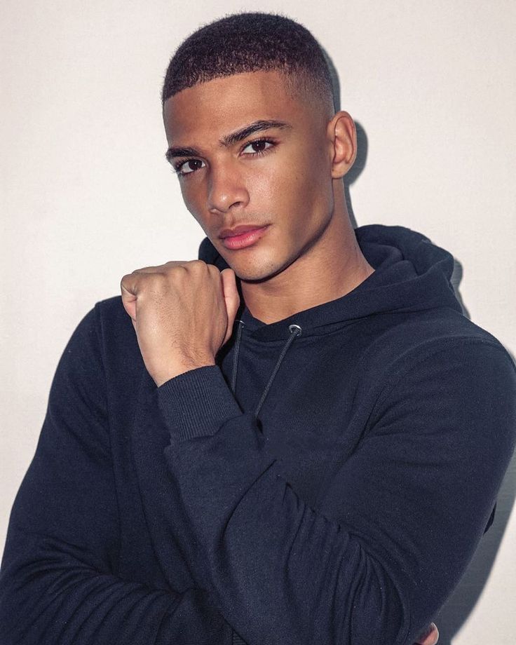 a young man in a hoodie posing for a photo with his arms crossed and looking at the camera