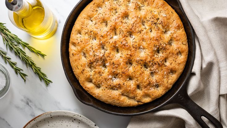 a pie in a cast iron skillet on a marble countertop next to olive oil and rosemary