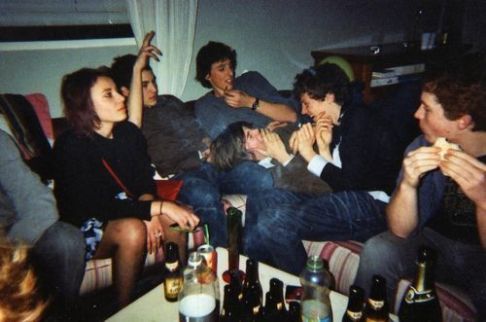 a group of people sitting on top of a couch eating pizza and drinking beer together