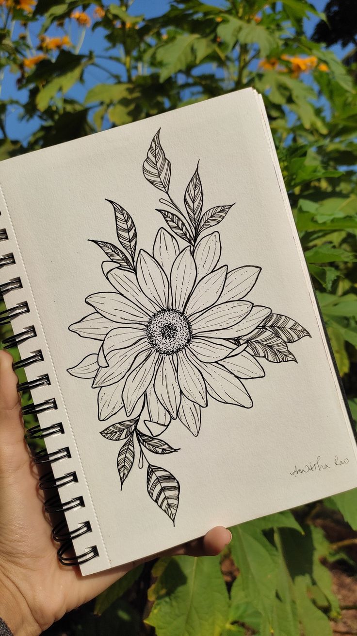 a person holding up a notebook with a drawing of a sunflower on it's cover