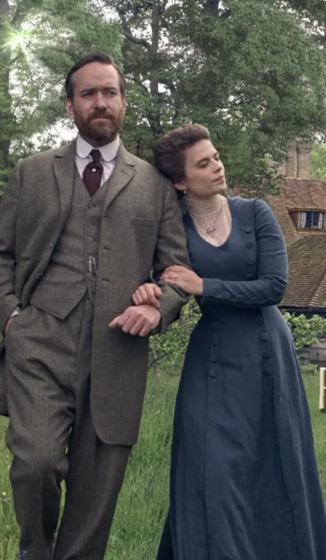 a man and woman standing next to each other in front of a forest filled with trees