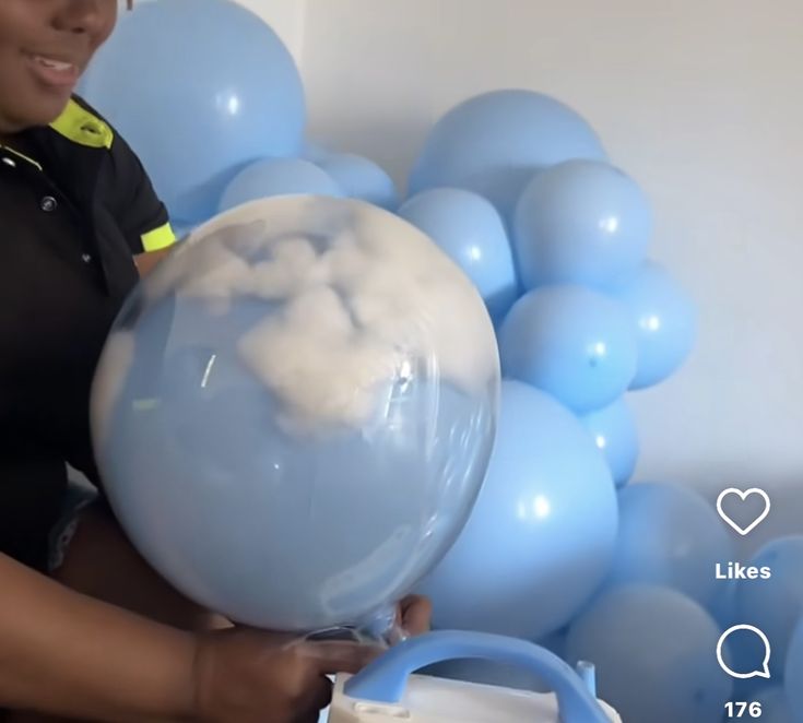 a woman holding a blue balloon in front of a bunch of balloons with clouds on them