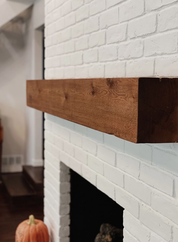 a white brick fireplace with a wooden mantle and two pumpkins sitting on the mantel