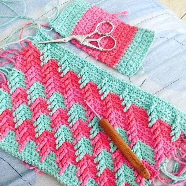 a pair of scissors sitting on top of a pink and green crocheted blanket