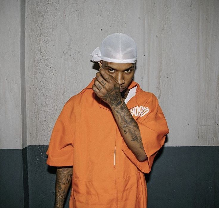 a man in an orange prison uniform covering his face