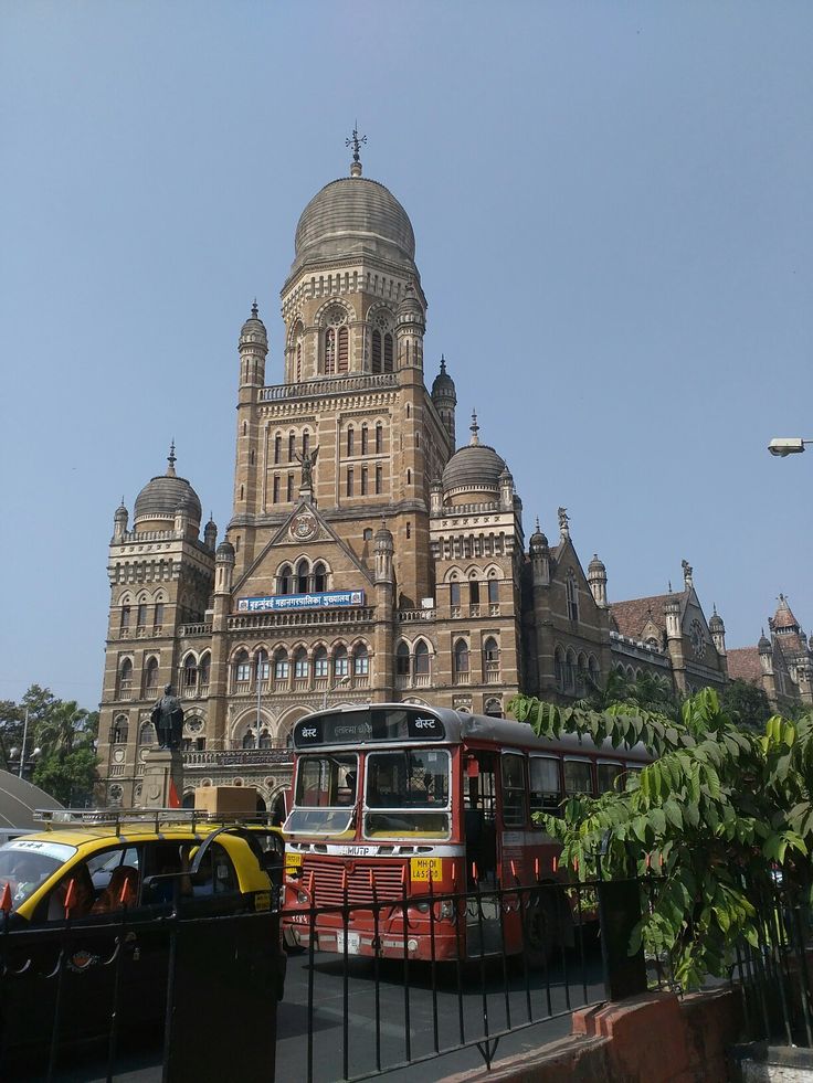 a red and yellow bus parked in front of a large building with a clock tower