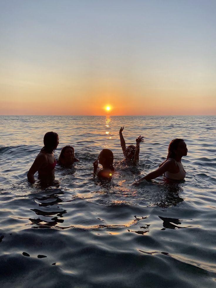 four people in the water at sunset with one raising their hand up to the sky