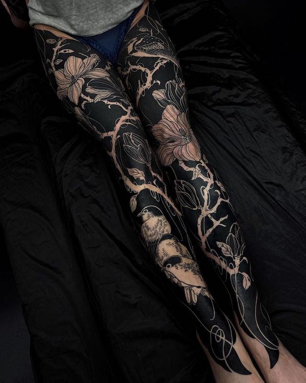 a woman with black and white tattoos on her legs is sitting on a bed in front of the camera