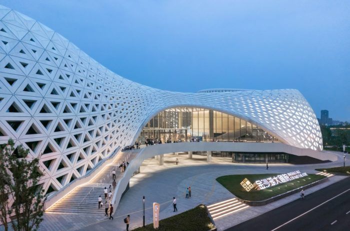 an architecturally designed building is lit up at night with people walking around the outside